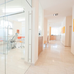 Helles, modernes Zahnarztpraxis-Wartezimmer mit Glastrennwand und orangefarbenen Akzenten.